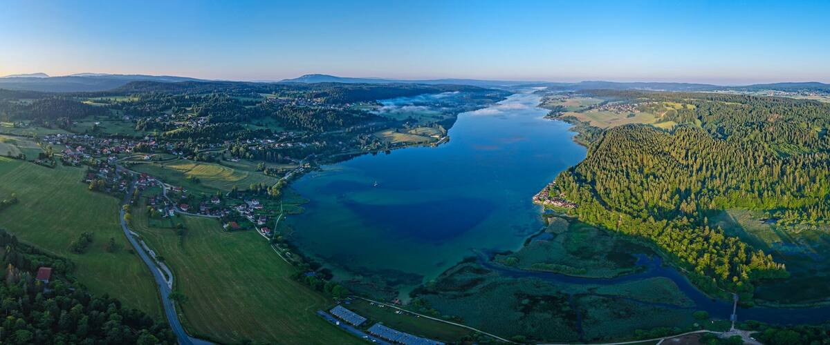A river winding through a valley with a town on one side and forested hills on the other.