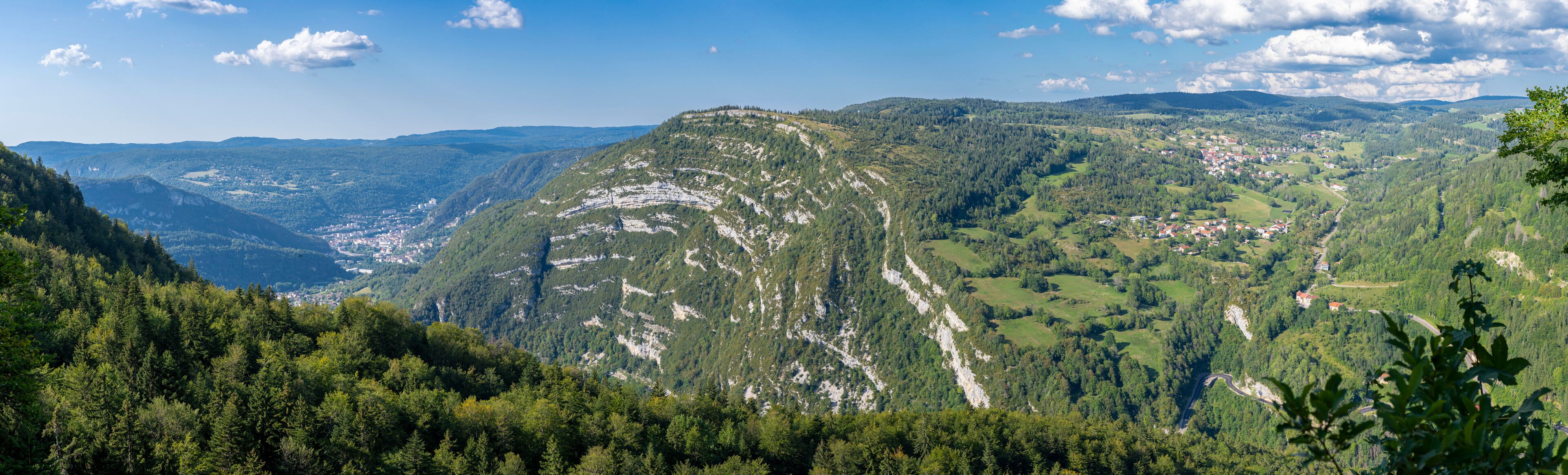 A mountainous landscape with dense forests, a winding road, and a small town nestled in the valley.