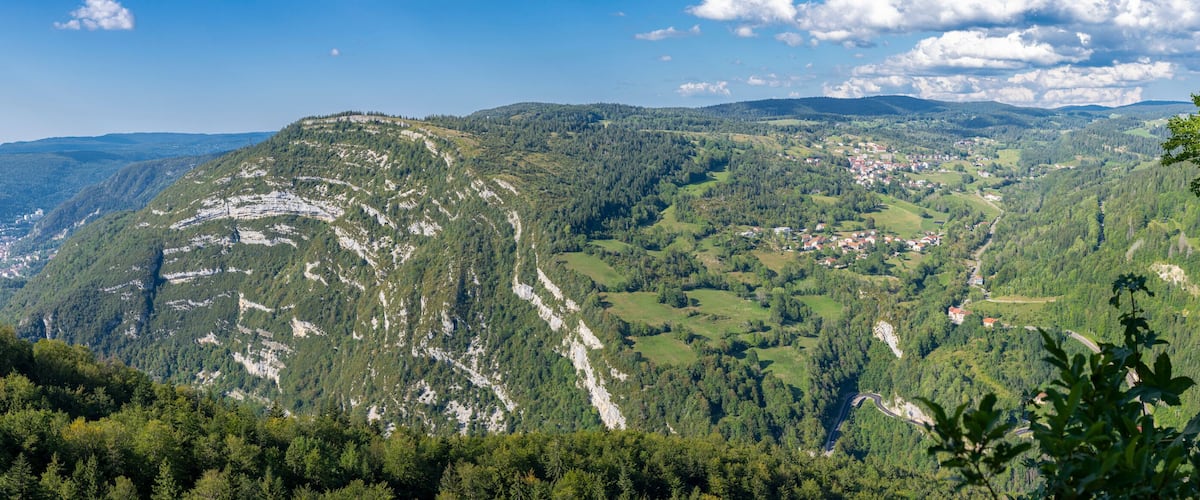 A mountainous landscape with dense forests, a winding road, and a small town nestled in the valley.