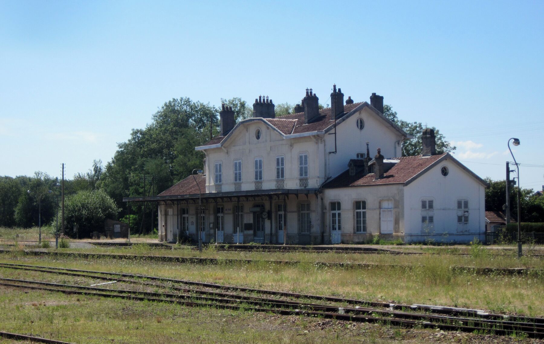 A white building with multiple chimneys, a balcony, and a roof with red tiles.