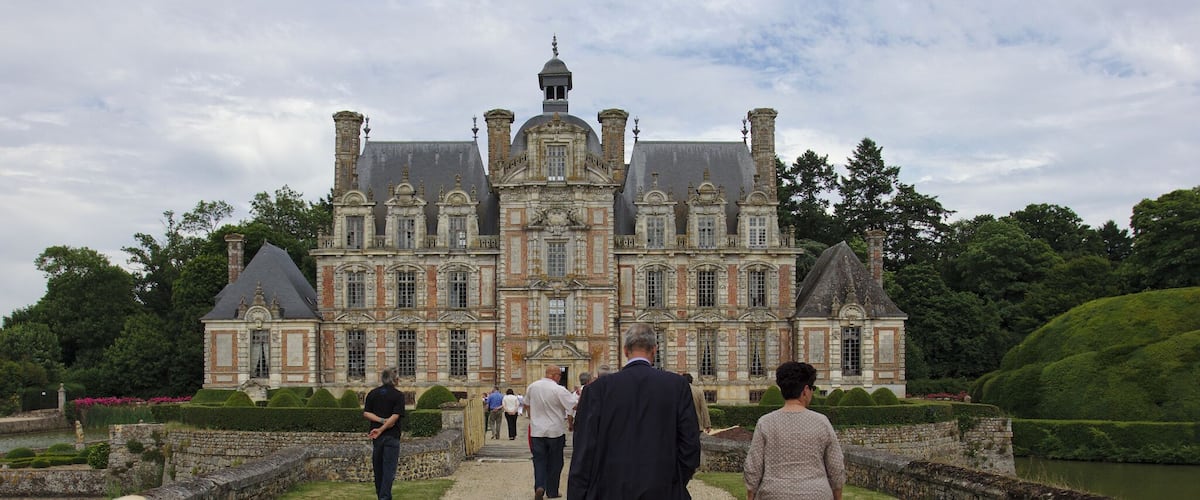 A grand château with a symmetrical facade, multiple chimneys, and a central dome.