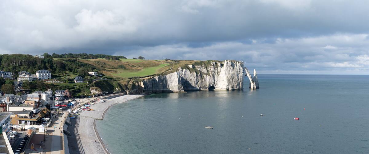 A coastal town with a prominent white cliff, a sandy beach, and a calm sea.