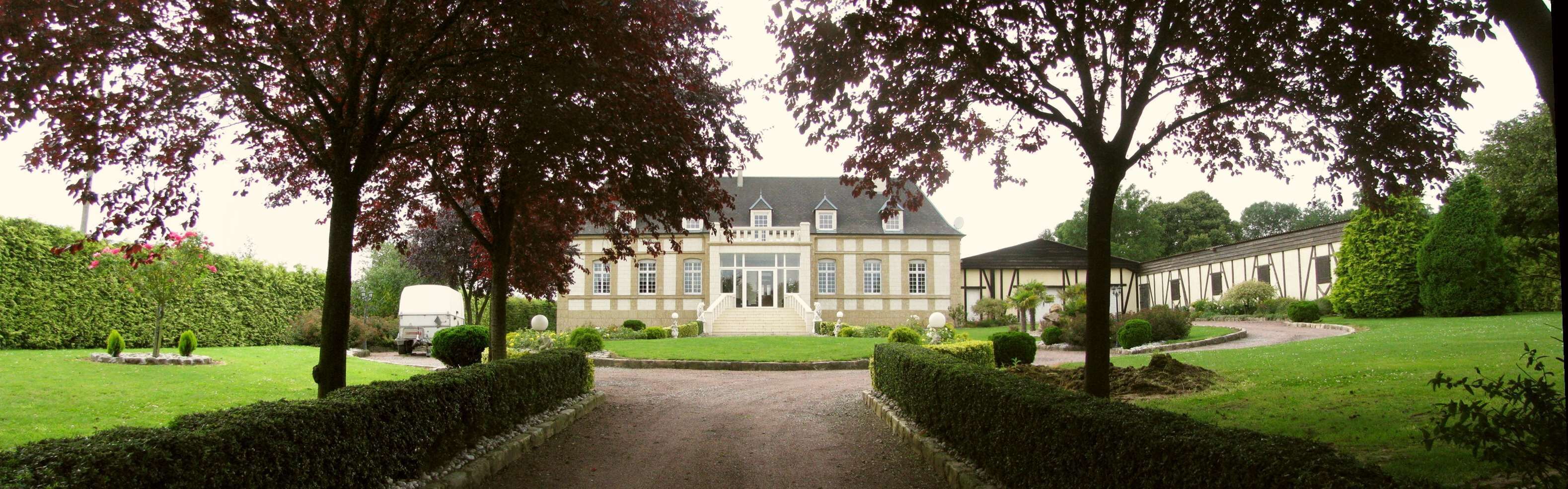 A large, historic building with a symmetrical facade, surrounded by well-manicured gardens and a gravel driveway.
