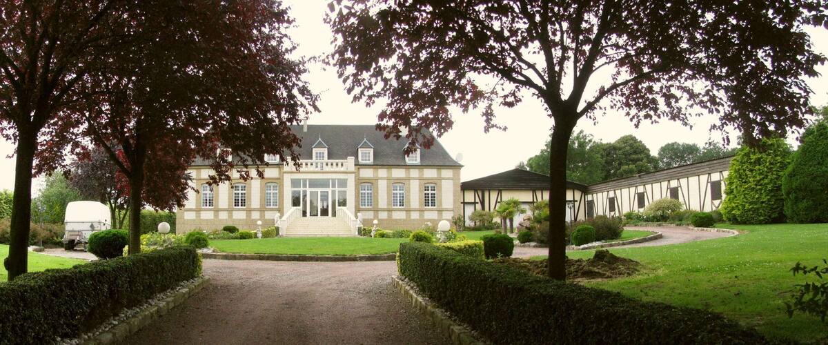 A large, historic building with a symmetrical facade, surrounded by well-manicured gardens and a gravel driveway.