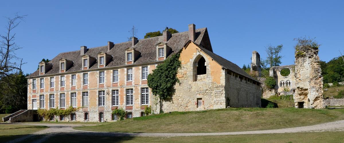 A historic building with a stone facade and multiple windows, surrounded by a grassy area and a stone ruin.