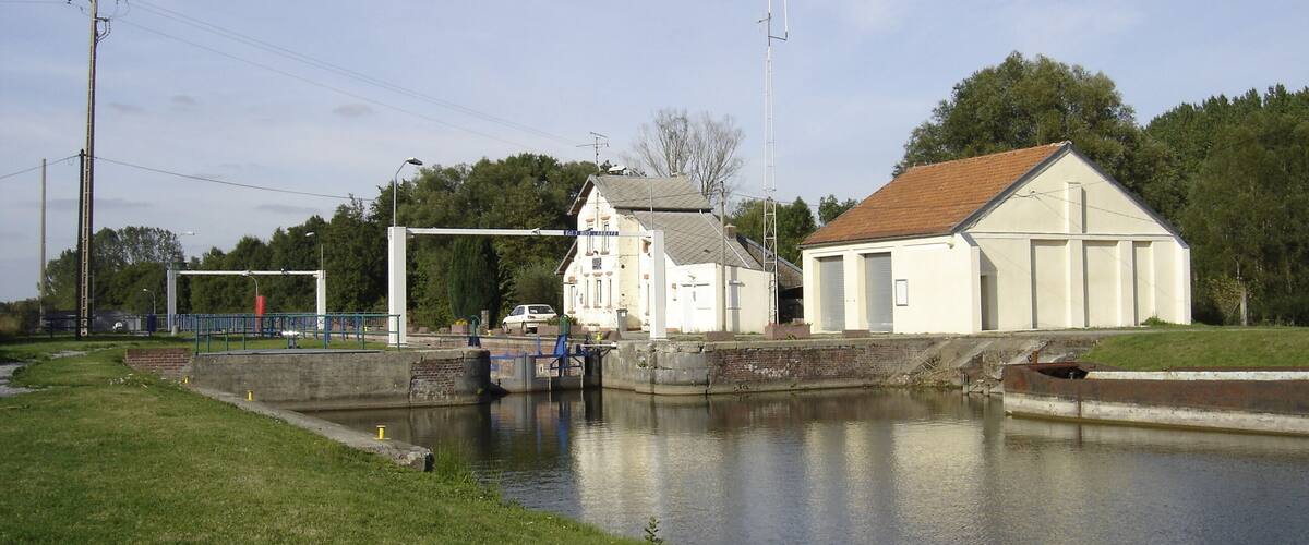 A canal with a lock system, a white building with a red roof, and a bridge in the background.