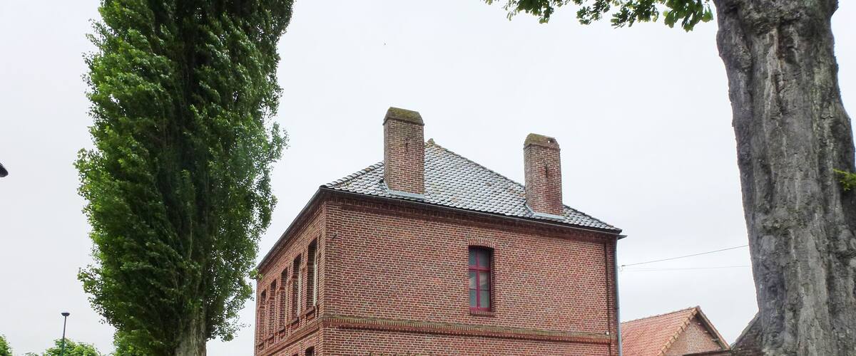 A brick building labeled "MAIRIE" with a red roof, surrounded by green grass, trees, and a bench.