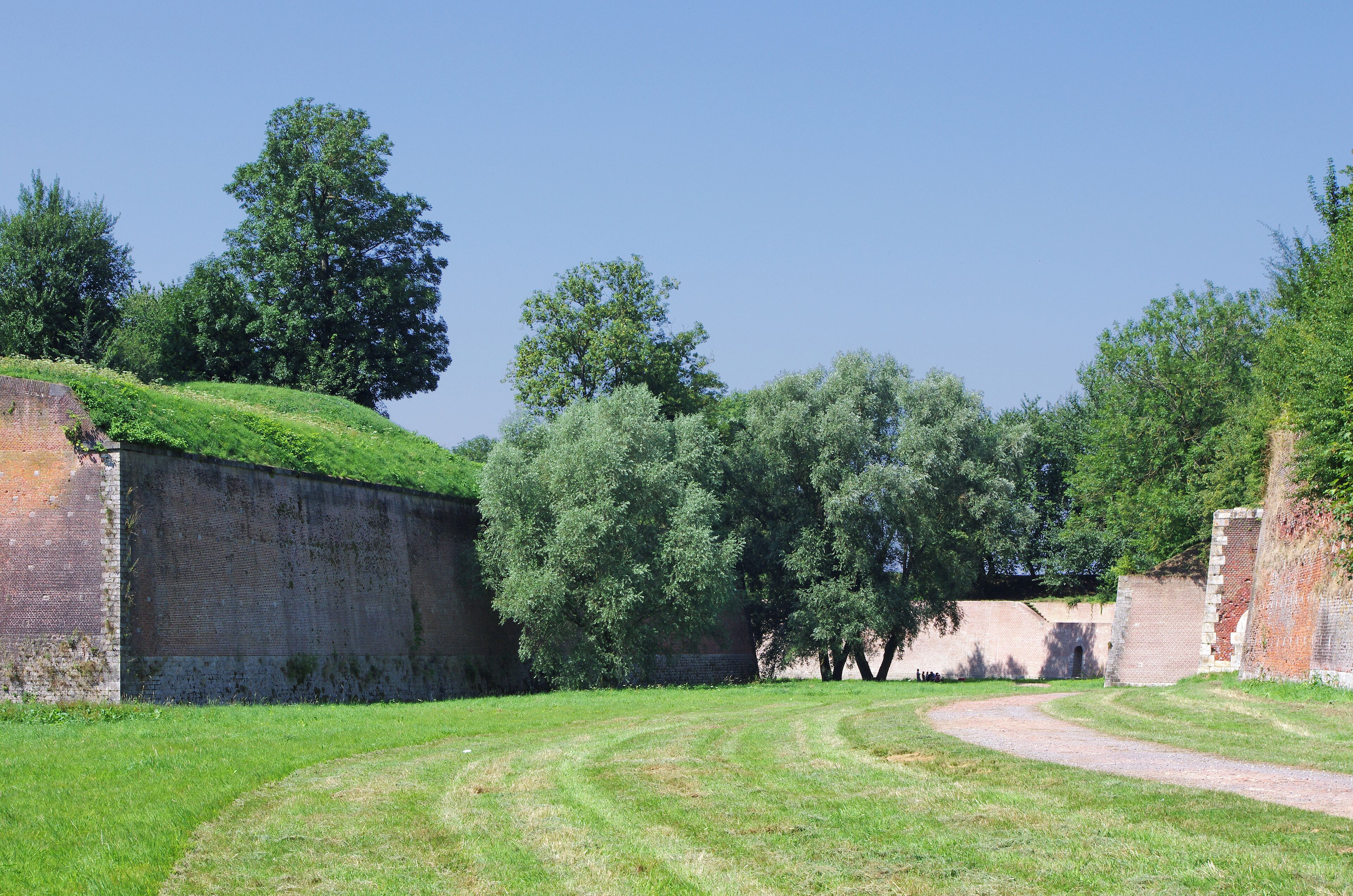 A grassy area with a curved path, brick walls, and trees.