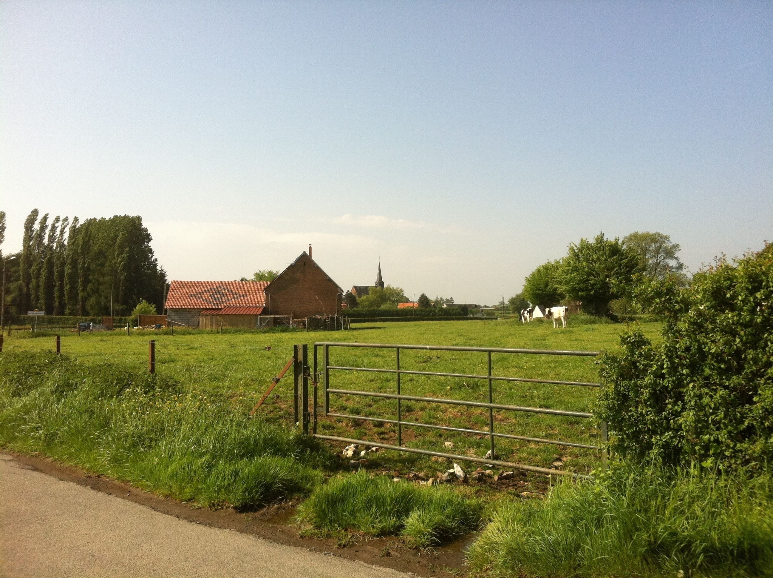 A rural landscape with a fenced field, a red-roofed barn, and a church steeple in the distance.
