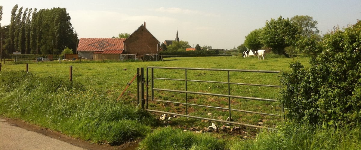 A rural landscape with a fenced field, a red-roofed barn, and a church steeple in the distance.