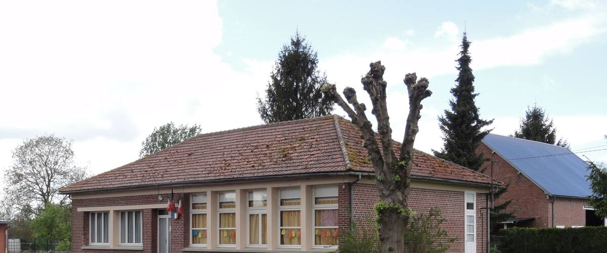 A brick house with a tiled roof, a gravel driveway, and a grassy yard with a tree.