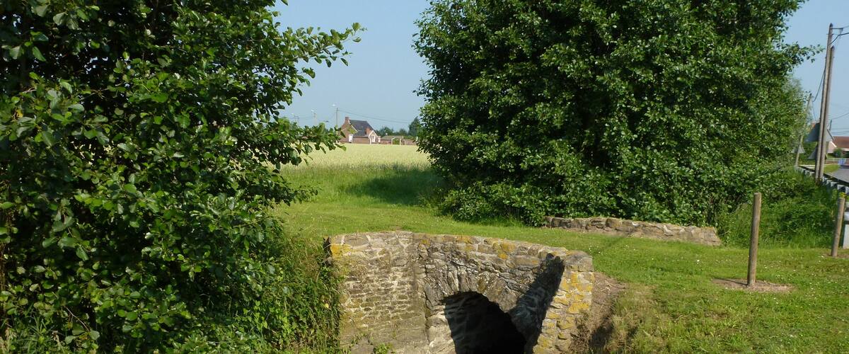 A stone bridge over a narrow water channel, surrounded by lush greenery and trees.