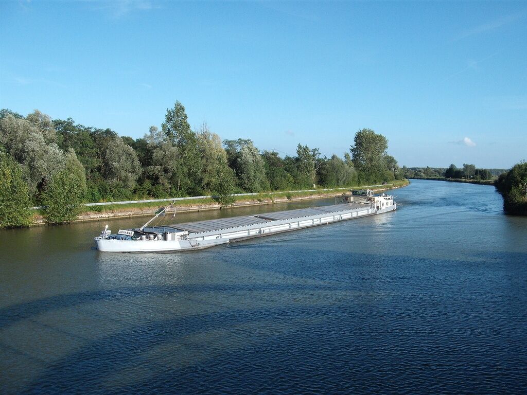 A large cargo ship on a river with a forested bank.