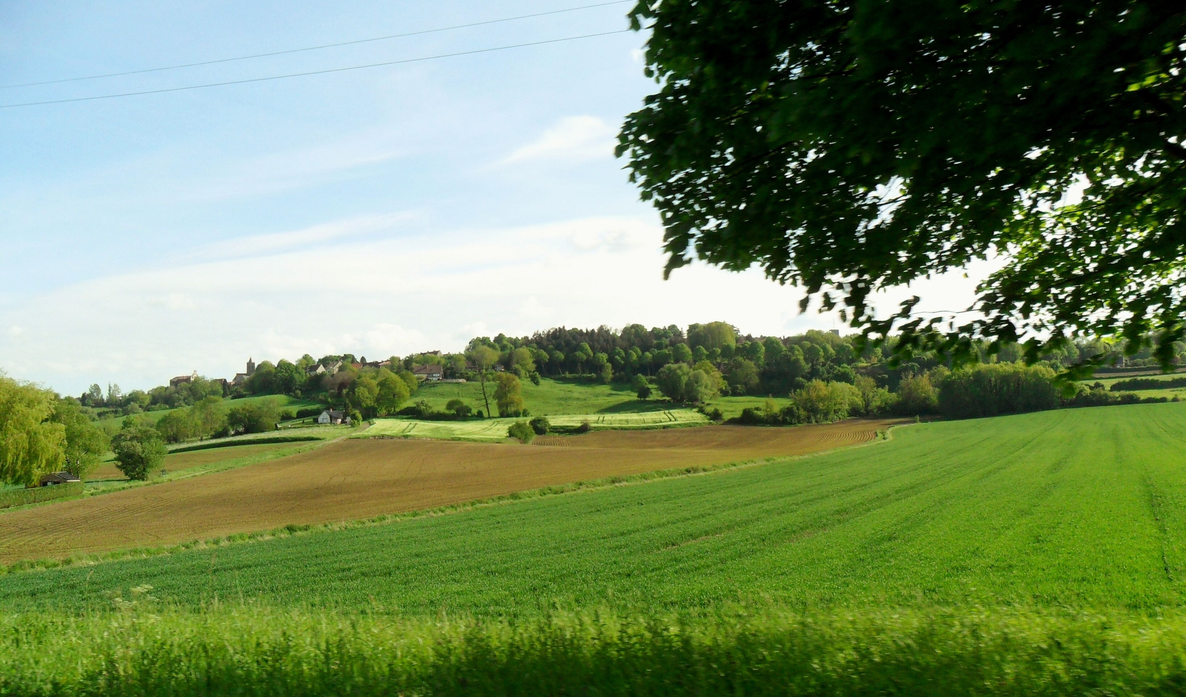 A rural landscape with rolling hills, fields, and a village in the distance.