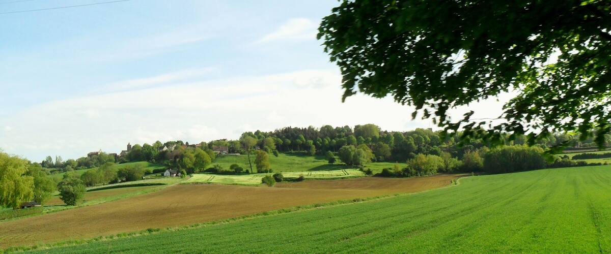 A rural landscape with rolling hills, fields, and a village in the distance.