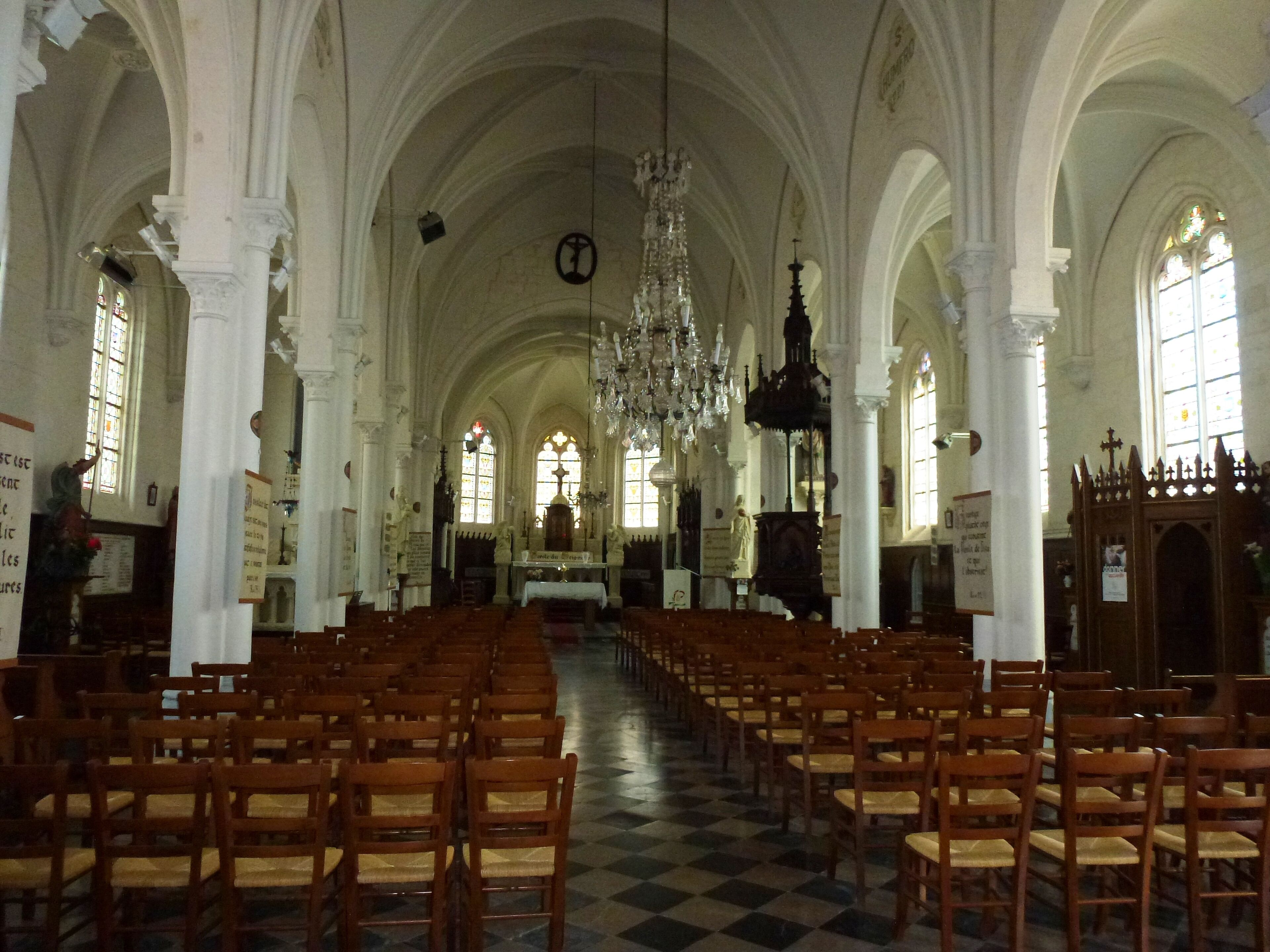 An interior of a church with wooden pews, a chandelier, and stained glass windows.