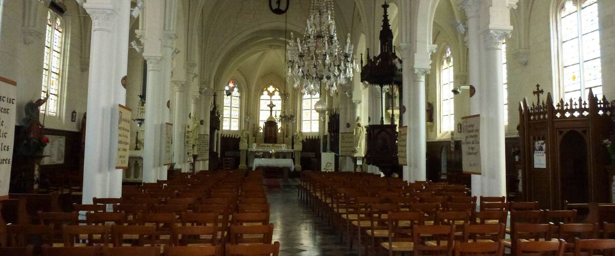 An interior of a church with wooden pews, a chandelier, and stained glass windows.