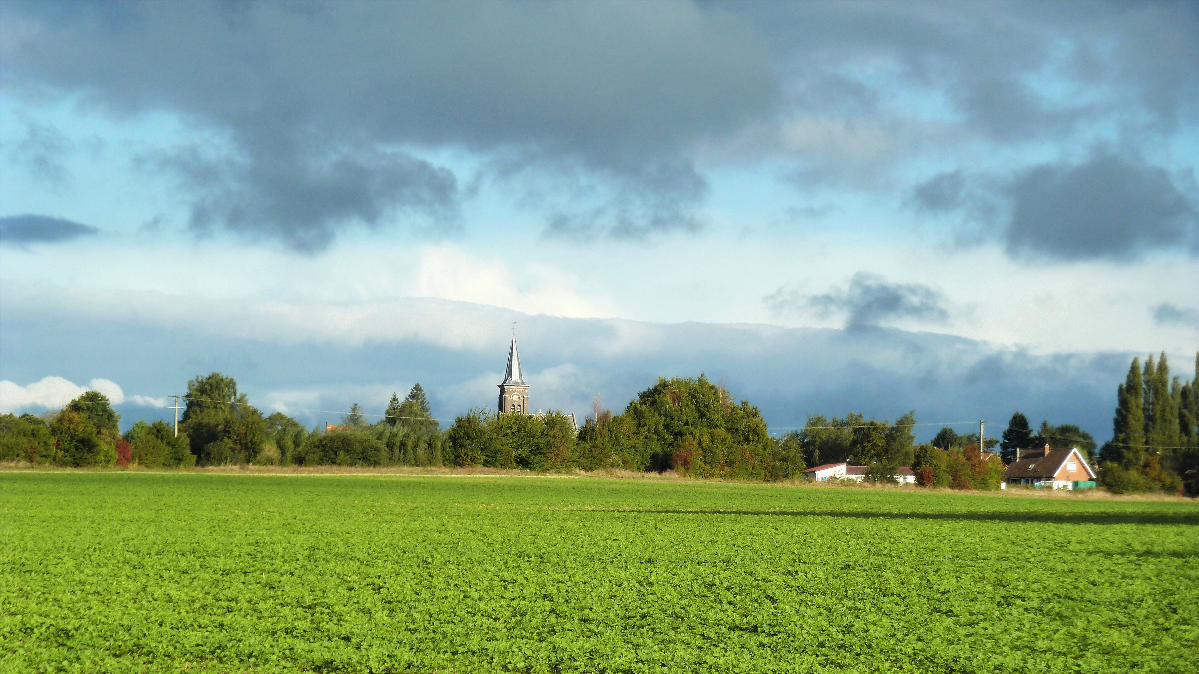 A green field, a church with a steeple, and a house in the distance.