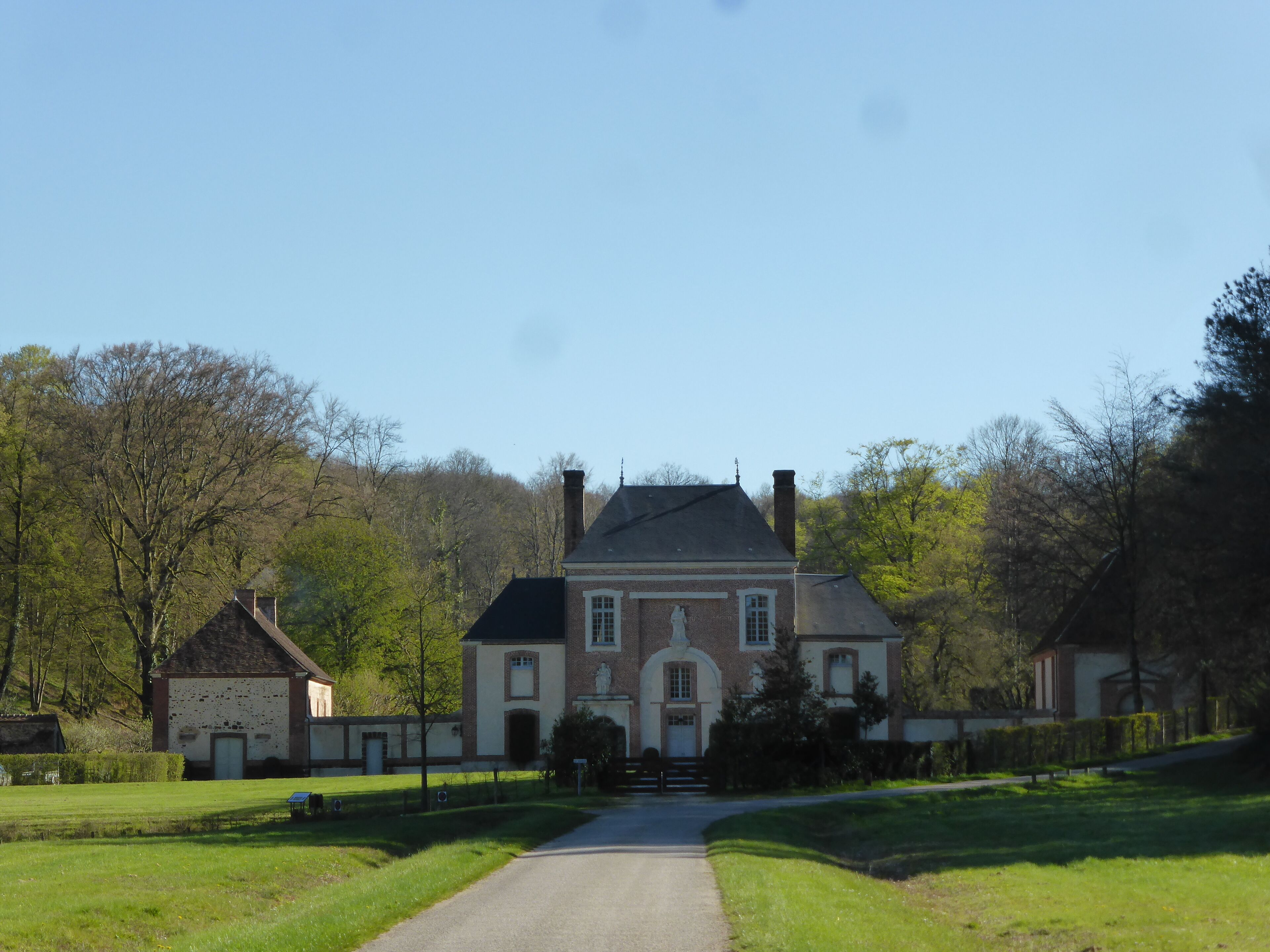 A large, historic house with a prominent statue in front, surrounded by lush green fields and trees.