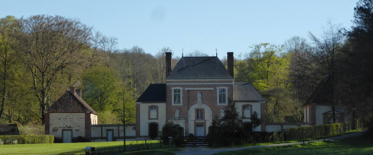 A large, historic house with a prominent statue in front, surrounded by lush green fields and trees.