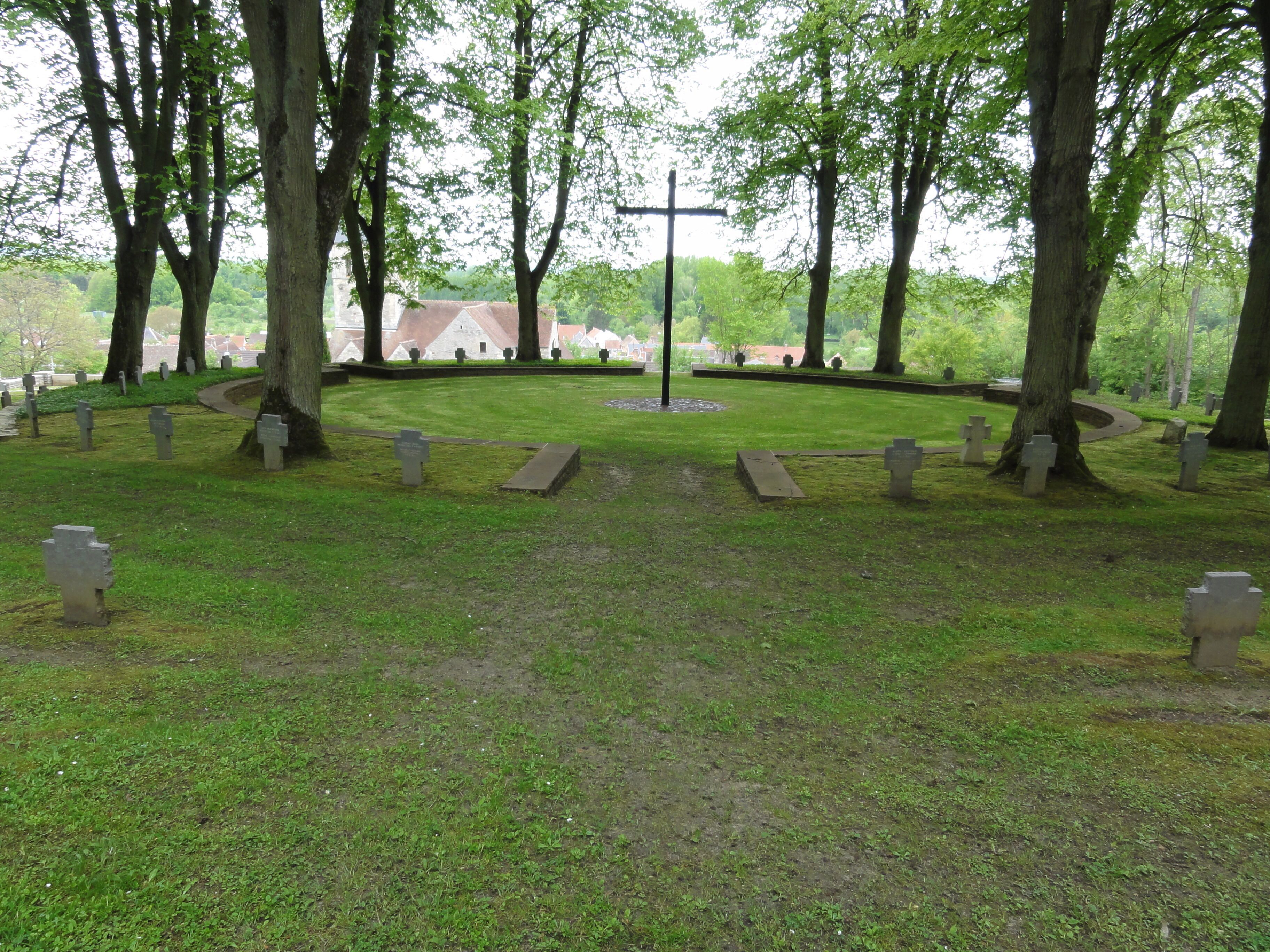 A cemetery with gravestones, trees, and a central monument.