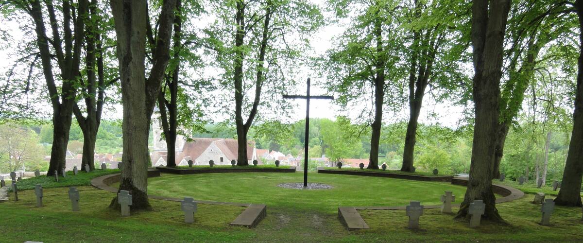 A cemetery with gravestones, trees, and a central monument.