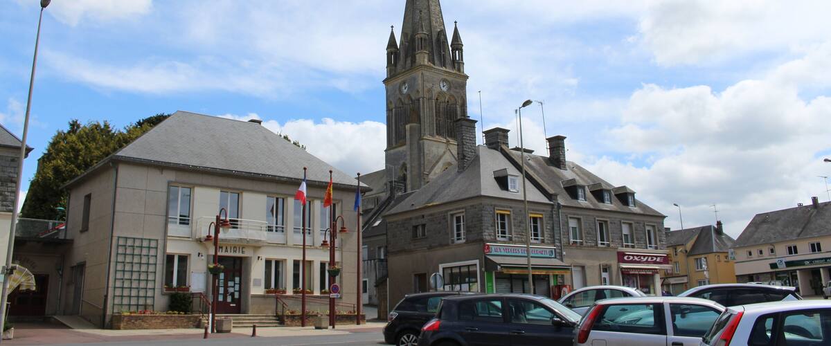 A church with a tall spire, a bakery, and parked cars in a town square.