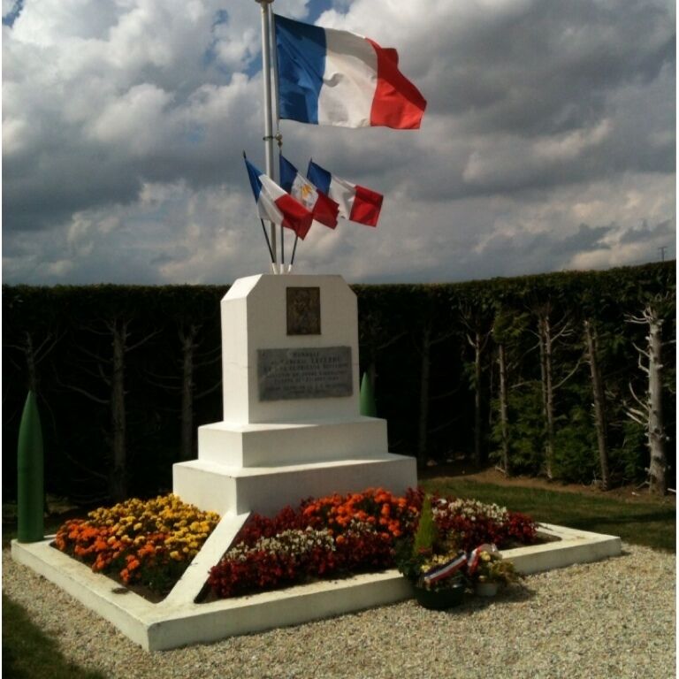 A memorial monument with flags, surrounded by flower beds.
