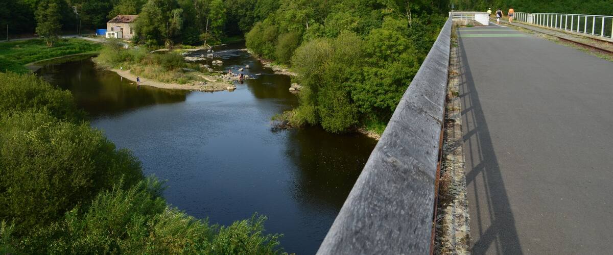 A bridge over a river with a small building on the left and dense greenery on both sides.
