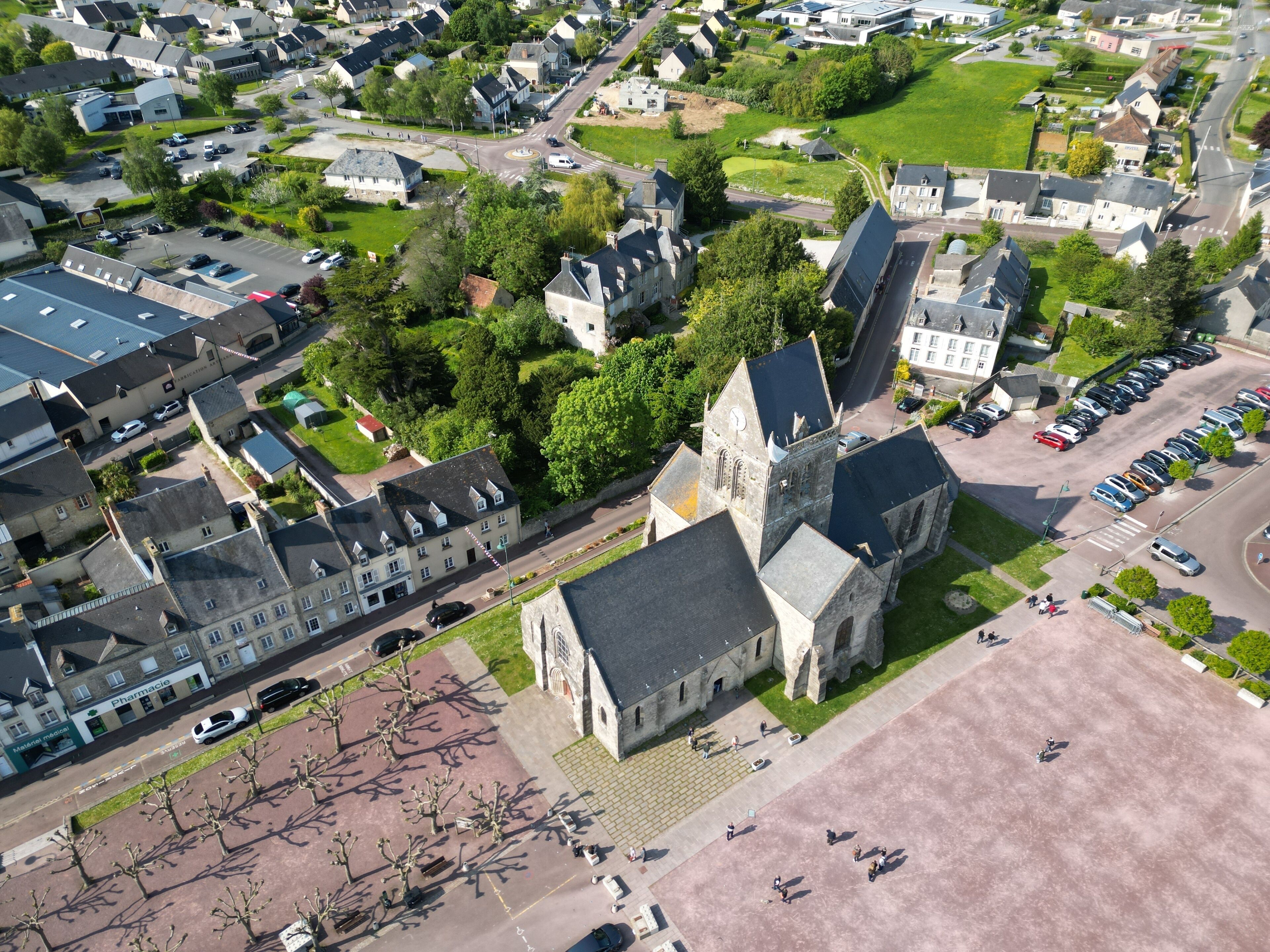 An aerial view of a town with a prominent church, residential houses, and a parking area.