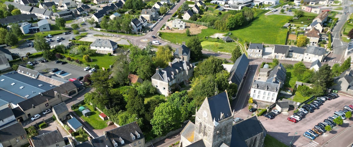 An aerial view of a town with a prominent church, residential houses, and a parking area.