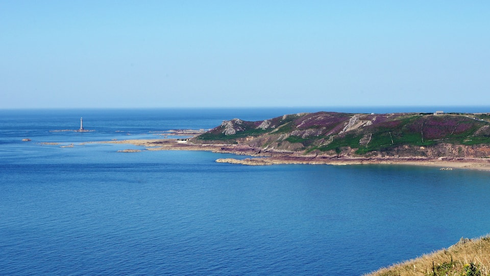 A coastal landscape with a lighthouse, rocky cliffs, and a clear blue sea.