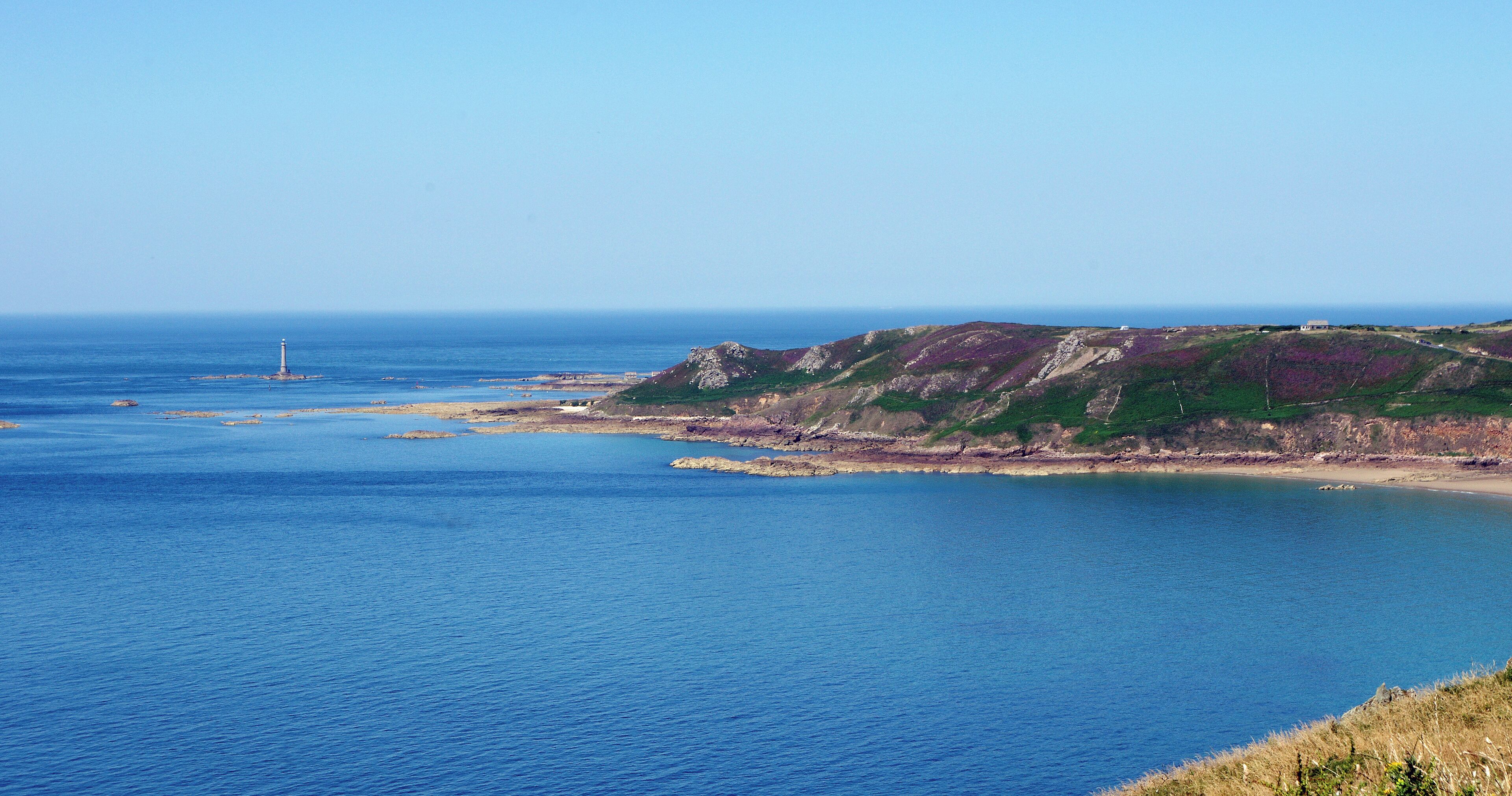 A coastal landscape with a lighthouse, rocky cliffs, and a clear blue sea.