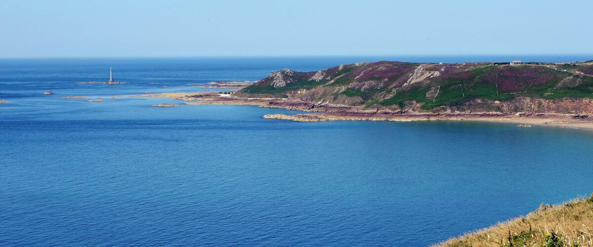 A coastal landscape with a lighthouse, rocky cliffs, and a clear blue sea.