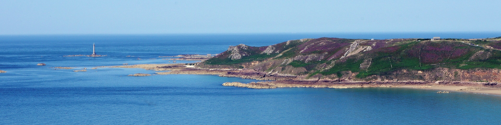 A coastal landscape with a lighthouse, rocky cliffs, and a clear blue sea.