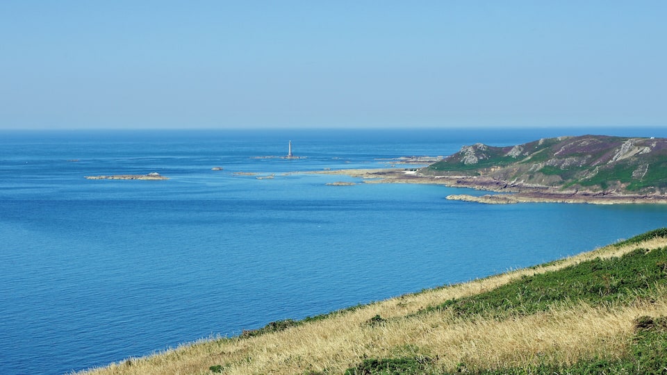 A coastal landscape with a lighthouse, rocky outcrops, and grassy hills.