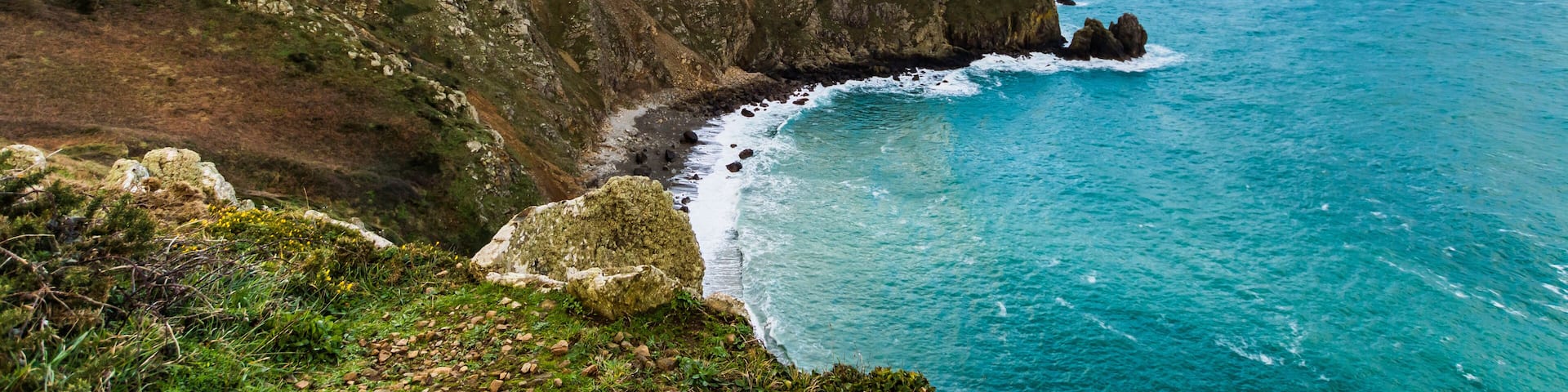 A coastal landscape with rocky cliffs, a clear blue sea, and a partly cloudy sky.