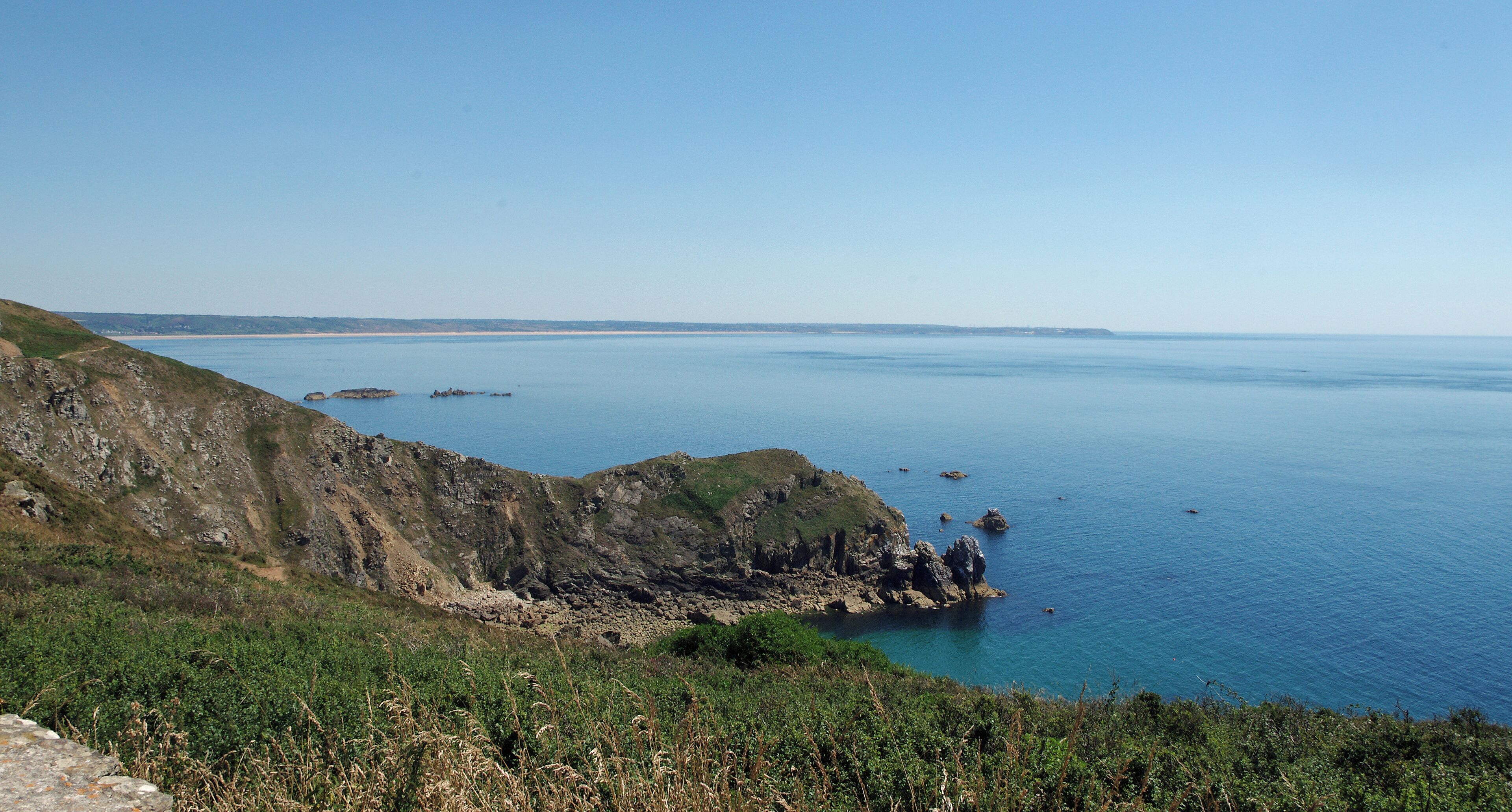 Jobourg (Manche) Le Nez de Jobourg vu depuis le Nez des Voidries. Entre les deux nez, l'Anse de Senival. Au loin, le Cap de Flamanville. "Nous dominons la mer de 128 mètres. A droite, nous avons le phare d'Auderville et le cap de la Hague ; à gauche l'anse de Vauville, que ferme dans le lointain, à une quinzaine de kilomètres, le cap de Flamanville. Une légère brume en haute mer nous cache les îles anglo-normandes. Tout près, au sud, s'allonge le Nez de Jobourg, moins haut mais plus déchiqueté que la pointe sur laquelle nous sommes. Là, finit le passage de la déroute et commence le Raz-Blanchard. Dans les hautes falaises de Jobourg existent des grottes d'un accès difficile : on y descend en suivant un sentier périlleux établi par le T. C. F. Si dangereux que soient ces parages pour la navigation il n'en ont pas moins été fréquentés par les fraudeurs. Il y avait autrefois dans la région des sociétés organisées pour la fraude du tabac. La configuration de la côte, riche en cachettes, facilitait ce trafic. Les fraudeurs, les «hagards», selon l'expression locale, sont devenus plus rares. Les lourdes amendes et la prison qui les menacent aujourd'hui ont presque entièrement arrêté leur fructueux commerce." Compte rendu de l'excursion faite par la Société Historique et Archéologique de l'Orne dans le Cotentin 29 Août — 2 Septembre 1927 - Caen, 26 janvier 1928. Camille de Mons..
