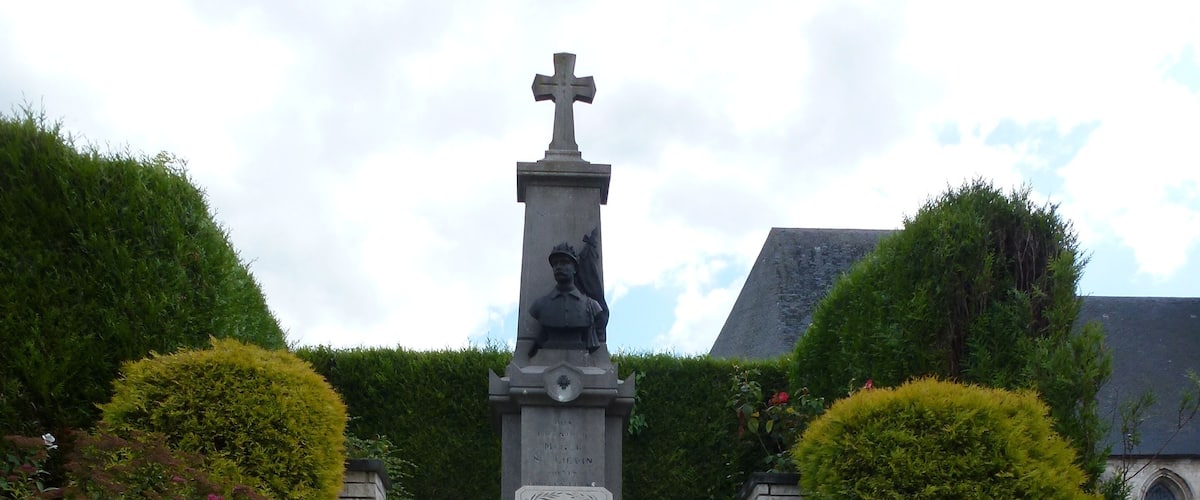 A set of stone steps leading up to a statue with a cross on top, surrounded by well-maintained hedges and flowering plants.
