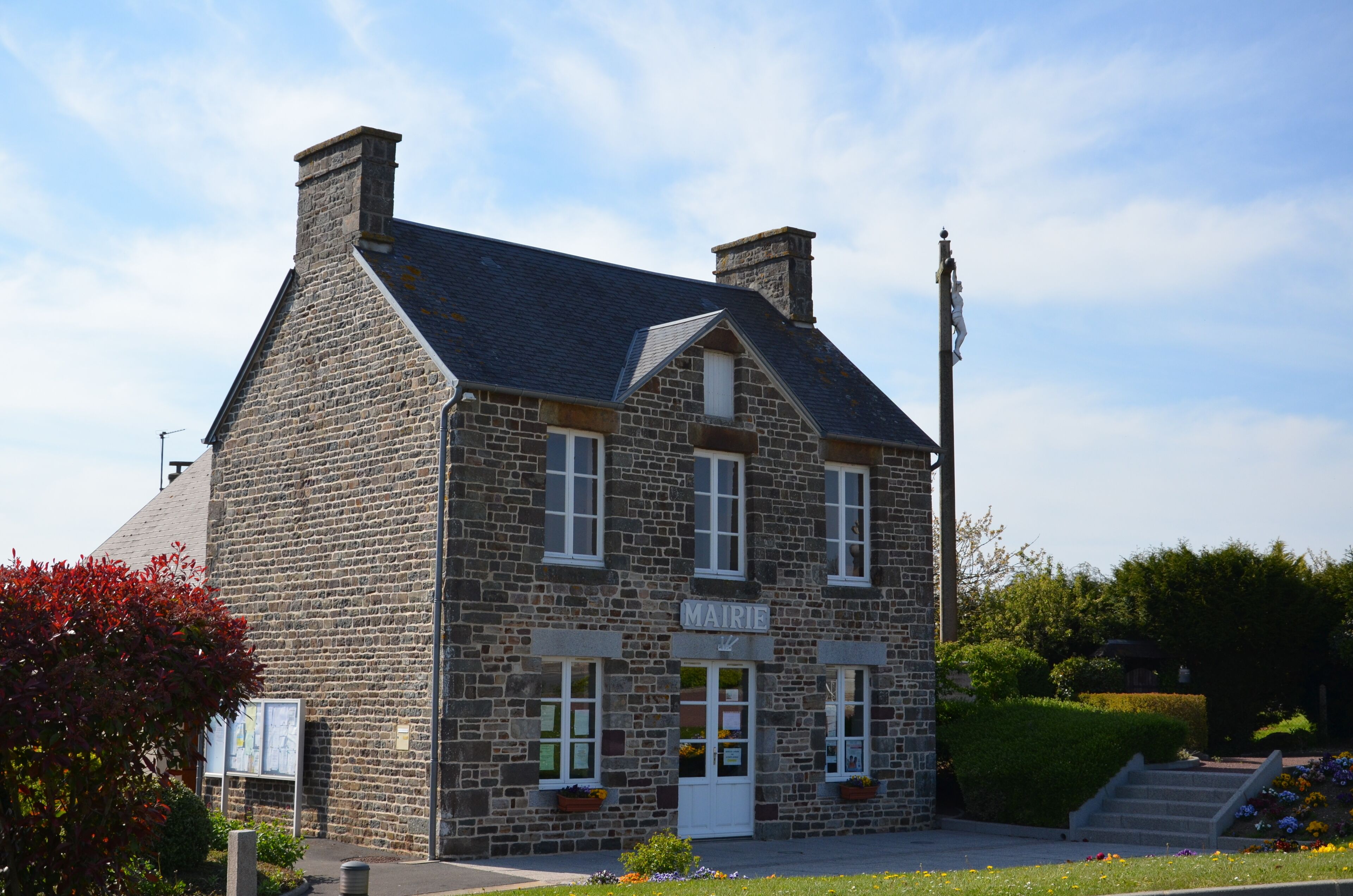 A stone building with a sign reading "MAIRIE" and a flagpole with a flag.