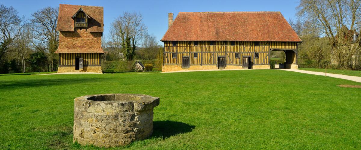 A historic building with a large barn and a tower, surrounded by a grassy field and trees.