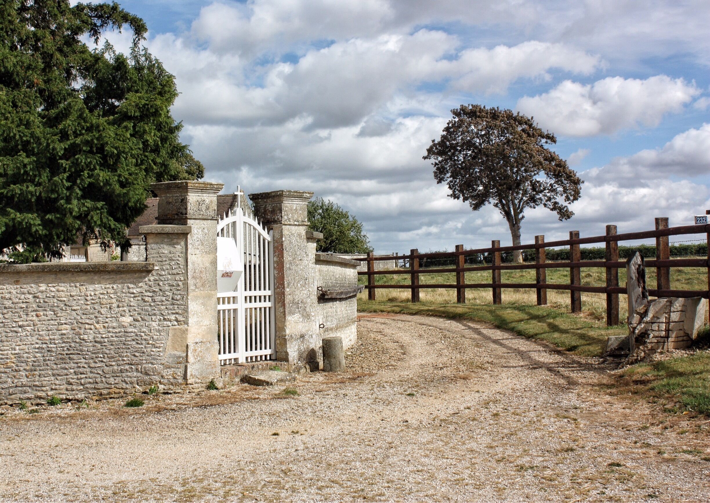 A stone wall, a white gate, a wooden fence, and a tree.