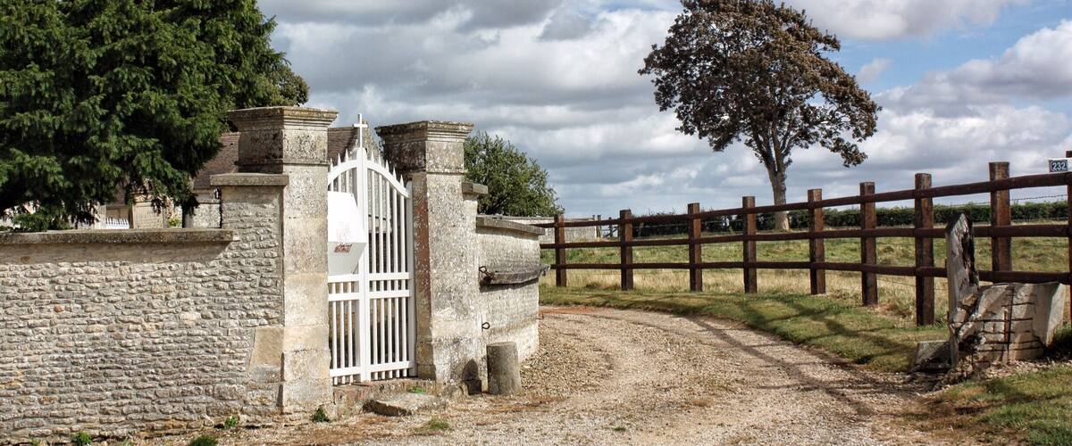 A stone wall, a white gate, a wooden fence, and a tree.