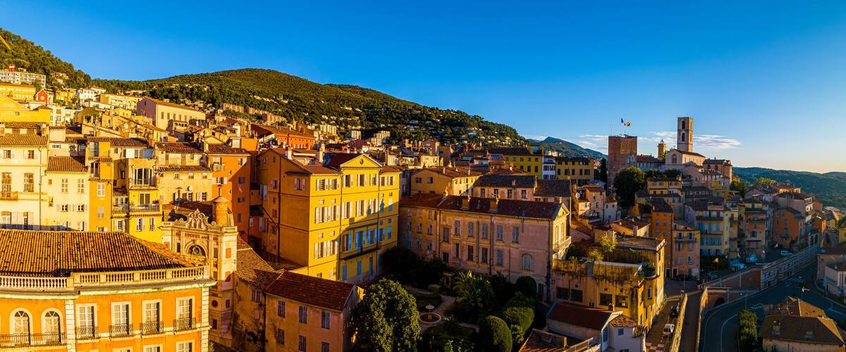 A historic town with colorful buildings, a prominent church, and a hill in the background.