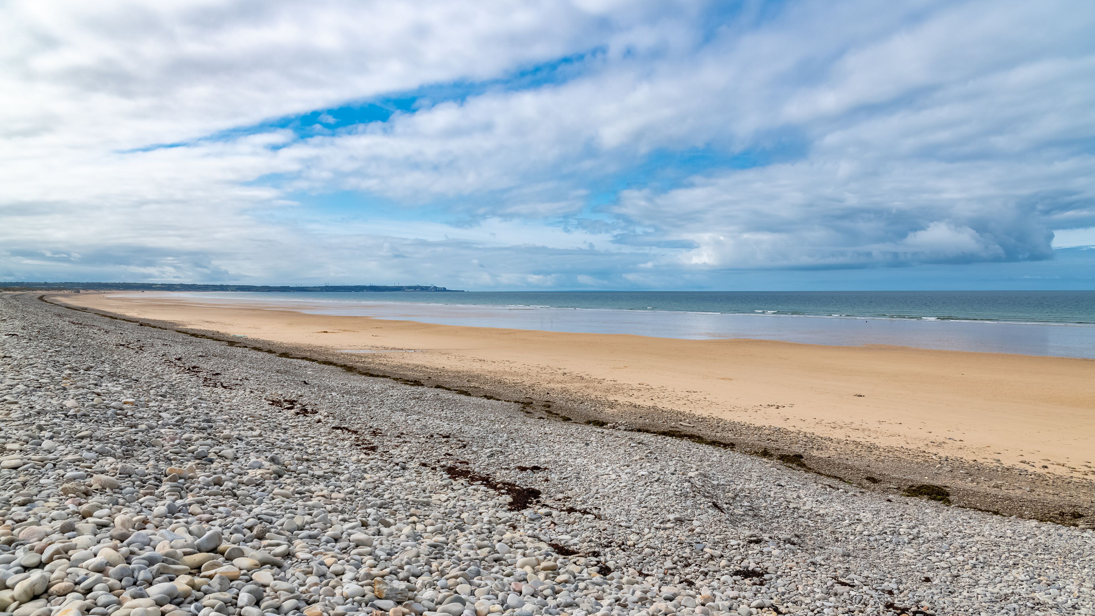 A pebbly beach with a sandy shore and a cloudy sky.