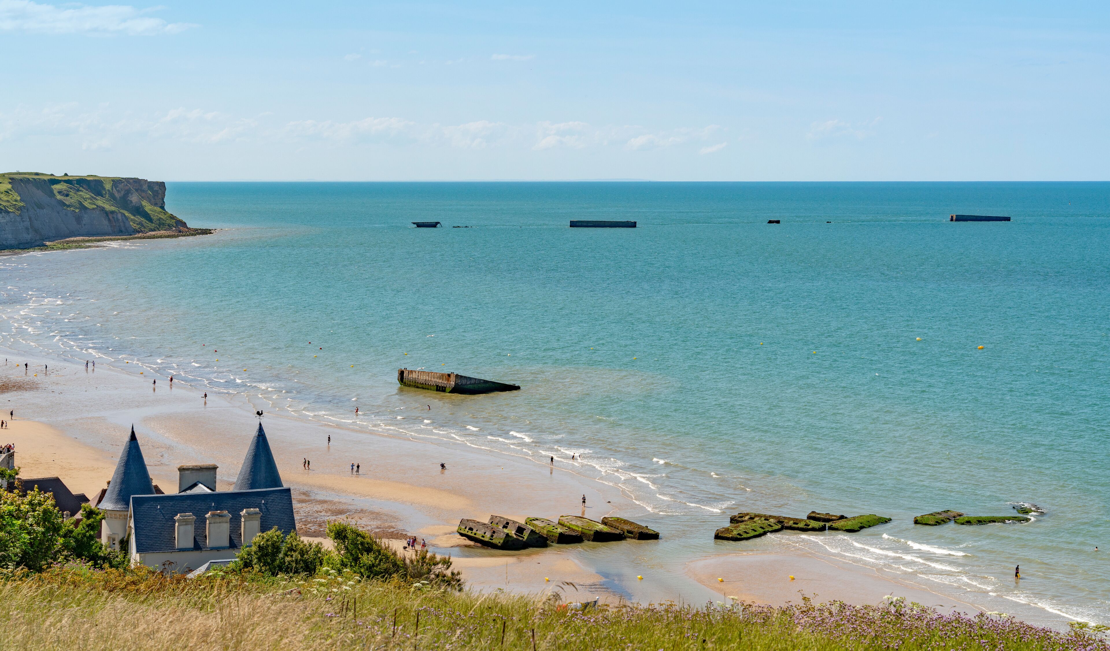 A coastal landscape with a sandy beach, a lighthouse, and a cliff.