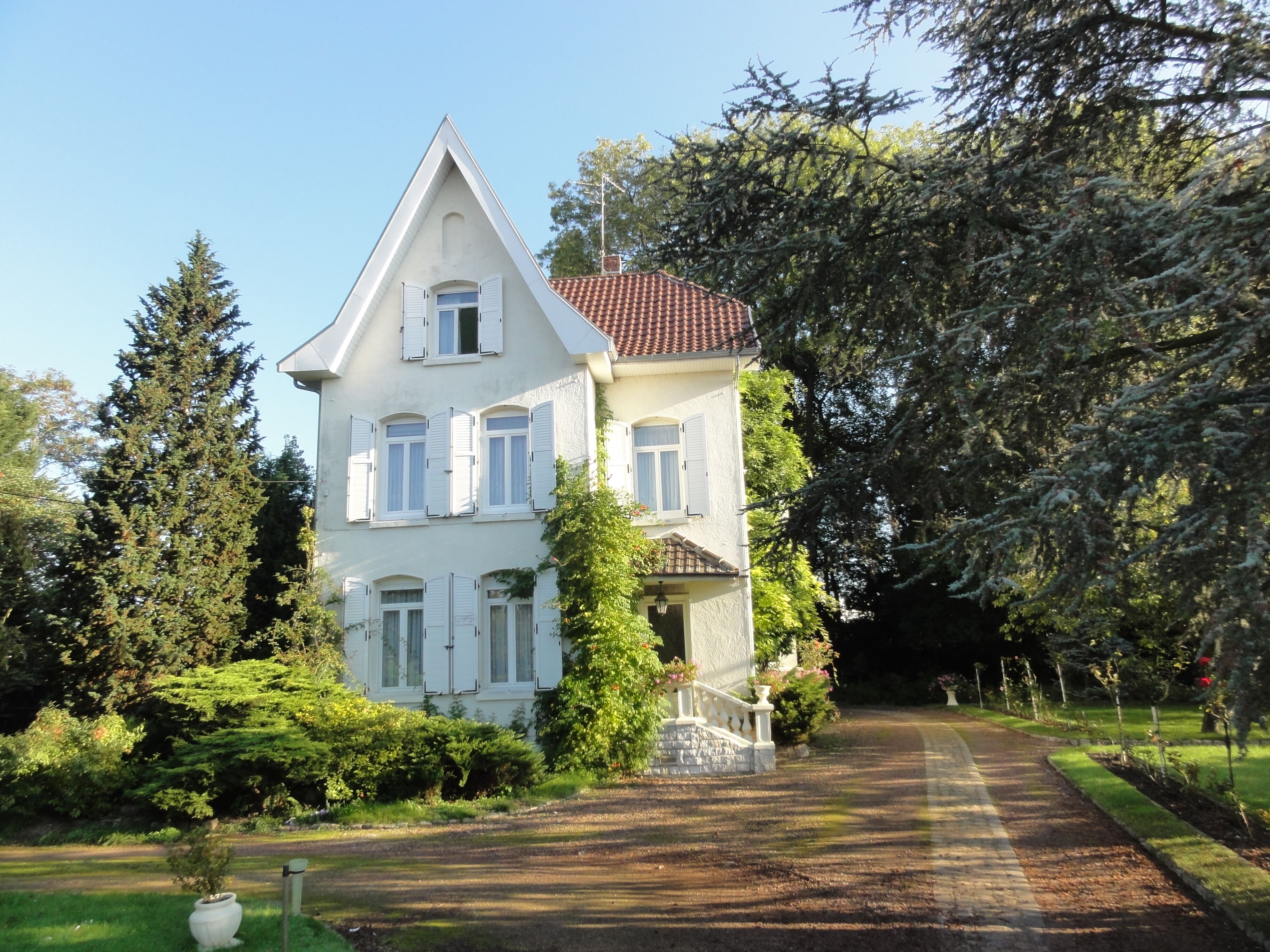 A white house with a red roof, surrounded by trees and a garden.
