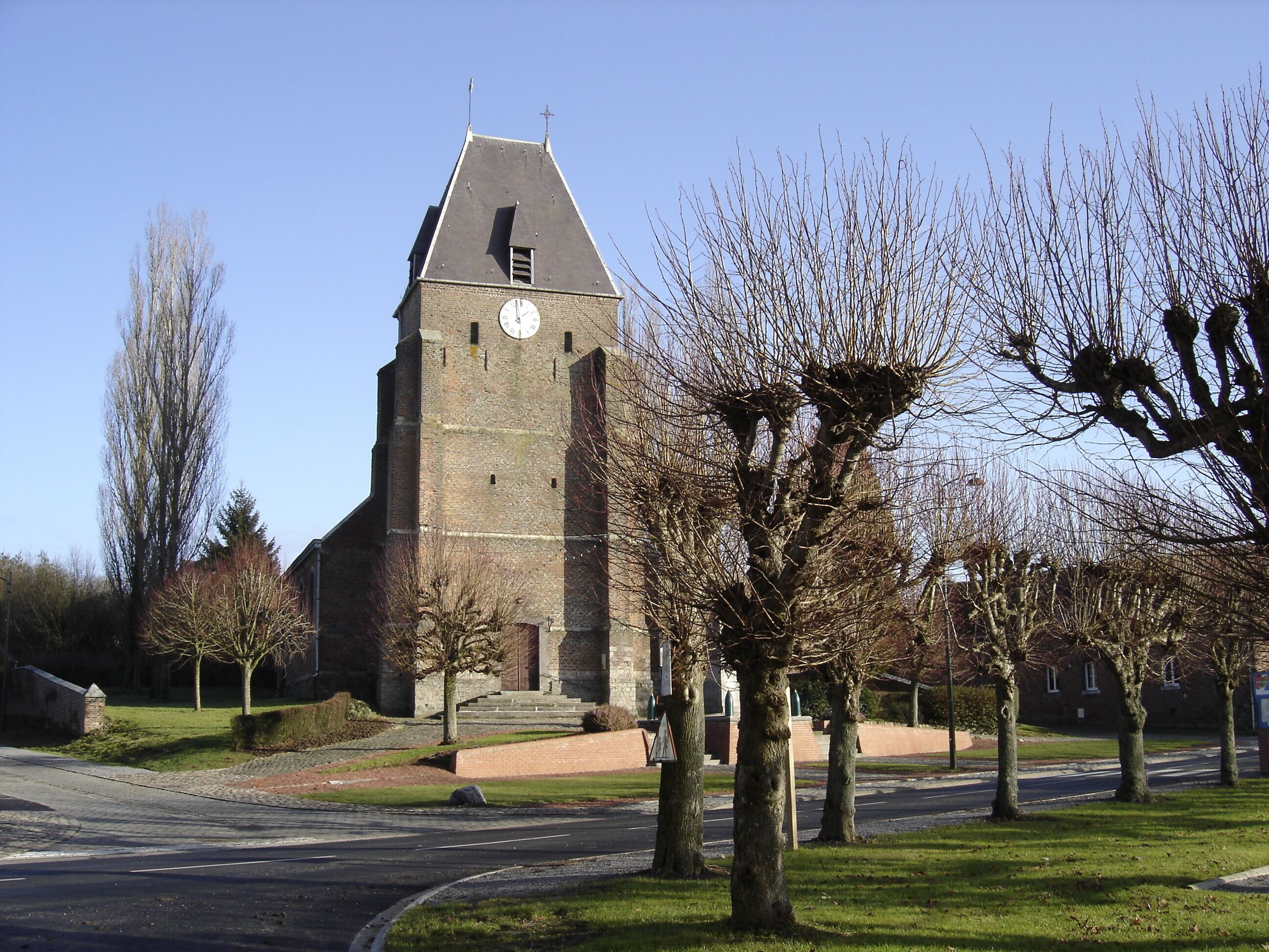 A church with a clock tower, surrounded by trees and a road.