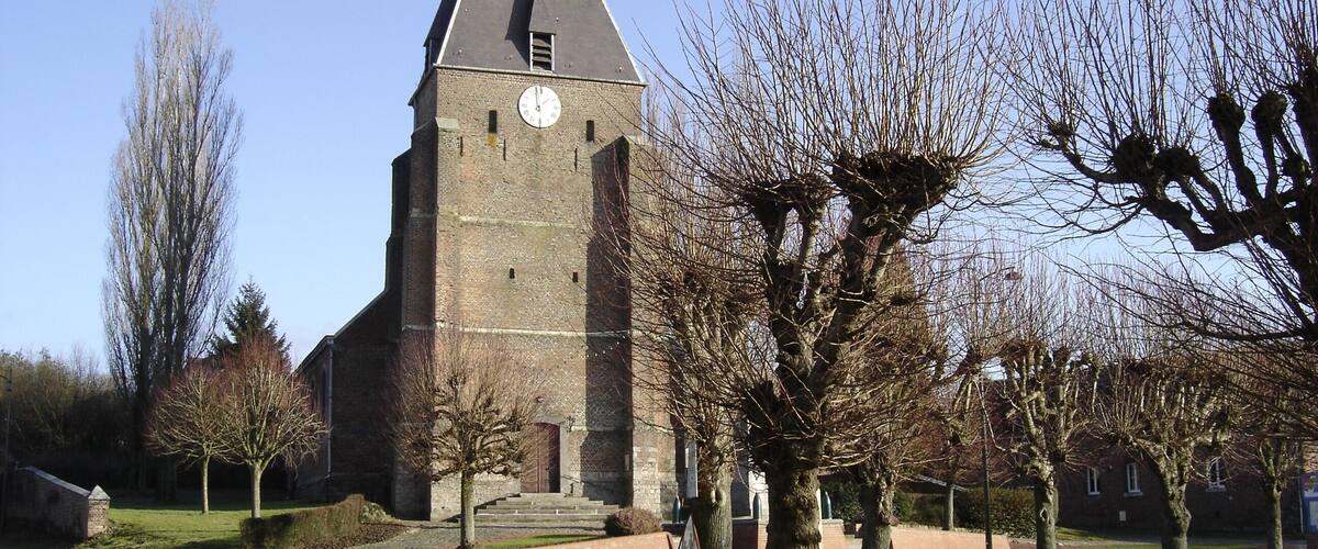 A church with a clock tower, surrounded by trees and a road.