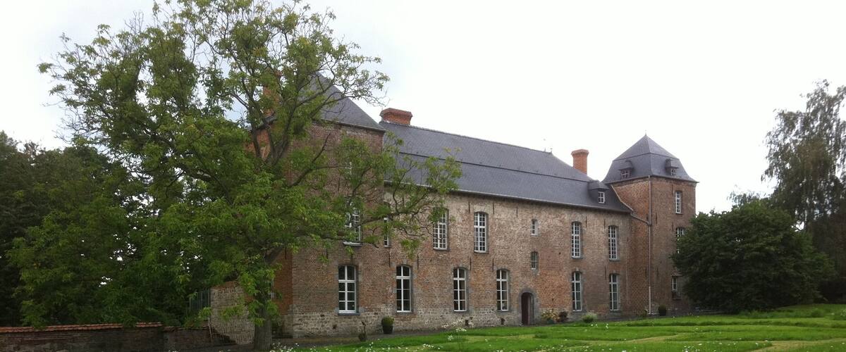 A large brick building with a tower, surrounded by a grassy field with white flowers.